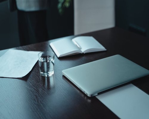 A notebook, pen, and a glass of water on a wooden table